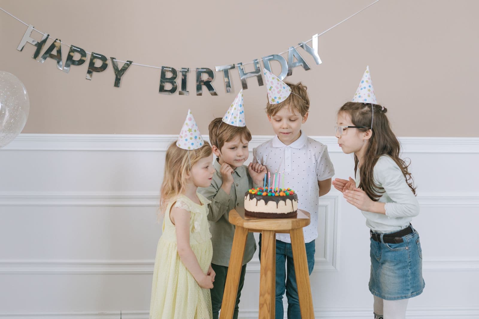 Kids in party hats gathered around a birthday cake